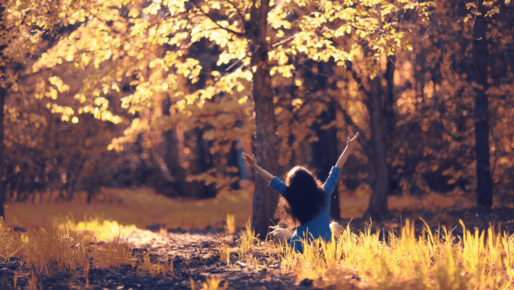 Femme assisse par terre dans une forêt aux couleurs d'automne